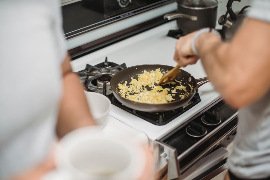 A person cooking eggs in a pan on a stovetop at home